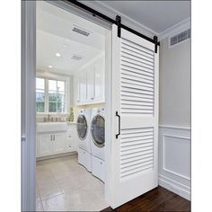 a washer and dryer in a large room with white walls, wood flooring and an open door leading to the bathroom