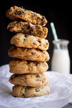 chocolate chip cookies stacked on top of each other with a glass of milk in the background