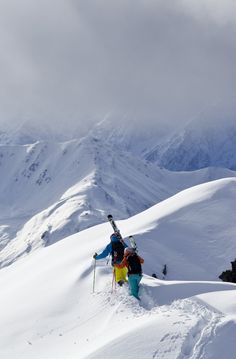 two skiers climbing up the side of a snow covered mountain