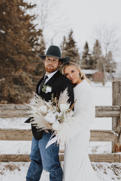 a bride and groom pose for a photo in front of a fence with snow on the ground