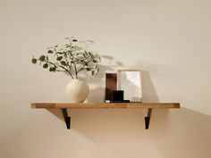 a white vase sitting on top of a wooden shelf next to a framed photo and plant