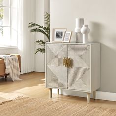 a white cabinet sitting in a living room next to a plant and pictures on the wall