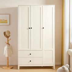 a white armoire sitting next to a window in a room with beige walls and wooden floors