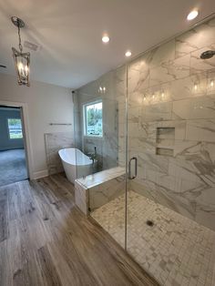 a bathroom with a glass shower door and white tub next to it on the wooden floor