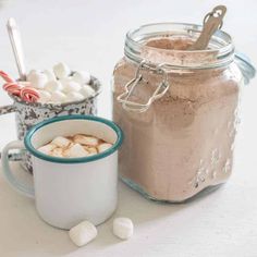 two mugs filled with hot chocolate and marshmallows sitting next to each other