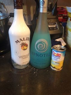 three bottles of alcohol sitting on top of a counter next to an electric blender