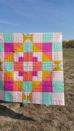 a colorful quilt is hanging on a clothes line in the middle of an open field