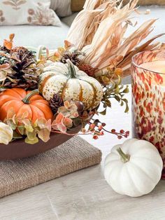 an arrangement of pumpkins, gourds and flowers on a table next to a candle