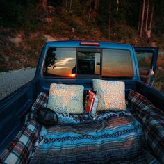 the back end of a truck with pillows and blankets in it's bed on the side of the road