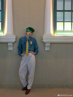 a man with green hair standing in front of two windows wearing white pants and a blue shirt