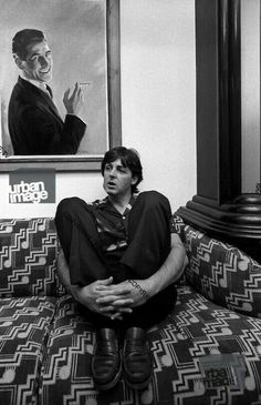 a man sitting on top of a couch in front of a framed portrait and painting