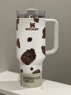 a white and brown travel mug with black dots on it sitting on a counter top