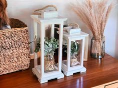 two white lanterns sitting on top of a wooden table next to a wicker basket