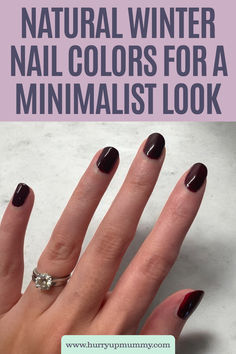 A hand with dark burgundy polished nails and a diamond ring showcases elegant fall nail colors 2024 against a minimalist background.