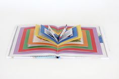 an open book with colored pages and pencil on top of it, sitting on a white surface