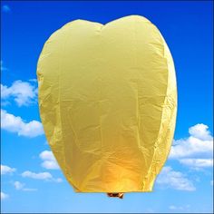 a yellow heart shaped hot air balloon flying in the blue sky with clouds behind it