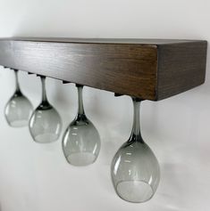 three wine glasses are hanging from a wooden shelf with glass holders on the wall behind them