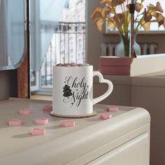 a coffee mug with pink marshmallows sitting on top of a white dresser