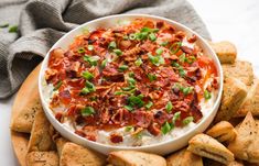 a bowl of dip with bacon and green onions on top surrounded by pita chips