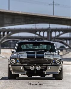 an old muscle car parked in front of a bridge