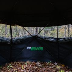 the big tent is set up in the woods with leaves on the ground around it