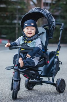 a baby in a batman costume is riding on a tricycle and smiling at the camera