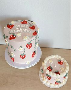 a pink birthday cake with strawberries on it next to a small white cupcake