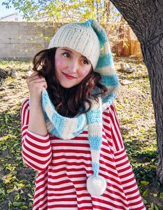 a woman wearing a hat and scarf in front of a tree with her hands on her hips