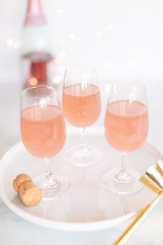 three glasses of pink wine on a white plate with gold spoons and a bottle in the background