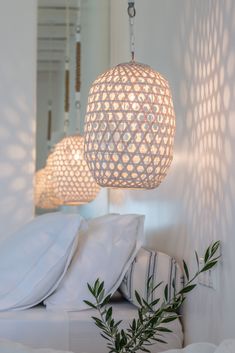 two lamps hanging from the ceiling above a bed with white sheets and pillows on it