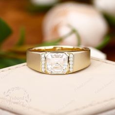 a gold ring with an emerald cut diamond on it sitting on top of a white box