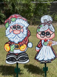 two santa and mrs claus yard signs in the grass