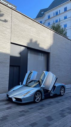 a silver sports car parked in front of a building with its doors open and the door opened