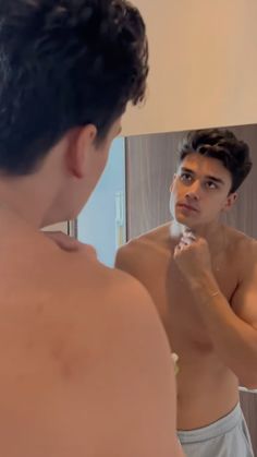 a man brushing his teeth in front of a mirror while looking at himself in the mirror