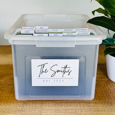 a plastic container filled with books on top of a wooden table next to a potted plant