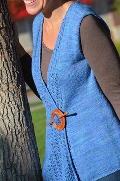 a woman standing next to a tree wearing a blue vest with an orange circle on it