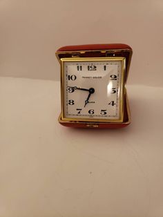 a small square clock sitting on top of a white table next to a red wall