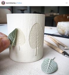 a cup with leaves on it sitting next to some crochet needles and yarn