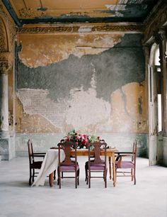 an old room with peeling paint on the walls and wooden chairs around a dining table