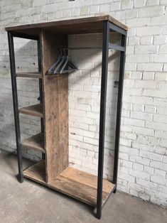 an industrial style wooden and metal shelf unit with clothes hanging on the rack, against a white brick wall