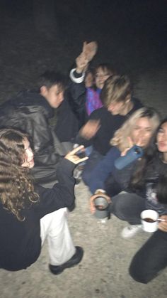 a group of people sitting on the ground at night with one person taking a selfie