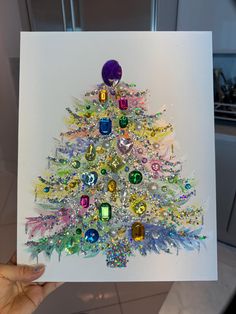 a hand holding up a card with a christmas tree made out of different colored jewels