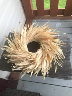 a wreath made out of dried corn sitting on a wooden porch with grass in the background