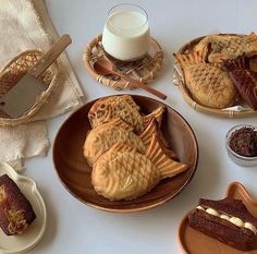 a table topped with plates and bowls filled with desserts next to a glass of milk