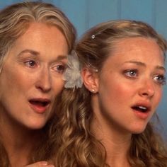 two women look surprised as they stand in front of a mirror