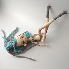 a doll with blue hair laying on top of a white table next to two sticks