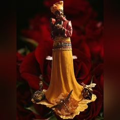 a figurine is sitting on top of a yellow dress and some red roses