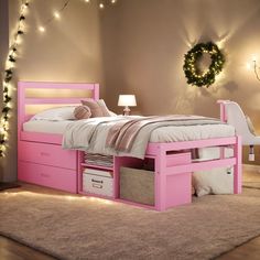 a pink bed with drawers underneath it in a room filled with lights and decorations on the wall