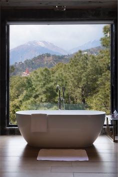 a white bath tub sitting in front of a window next to a forest filled with trees