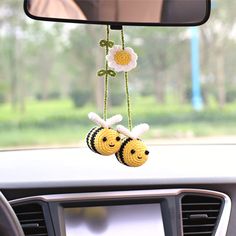 two crocheted bees hanging from the dashboard of a car with flowers on it